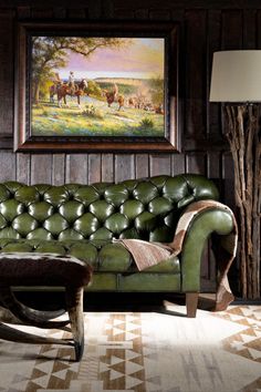 a green leather couch sitting in front of a painting on the wall next to a lamp