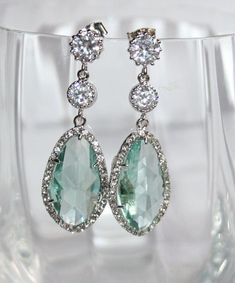 a pair of green and white stone earrings on a clear glass vase with water in the background