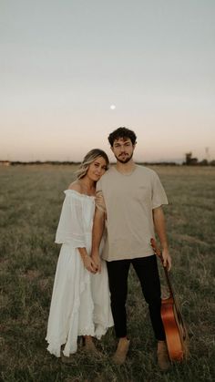 a man and woman standing next to each other in a field with an acoustic guitar