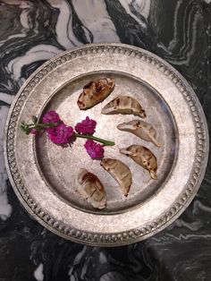 several pieces of food on a silver plate with purple flowers in the middle and marble background