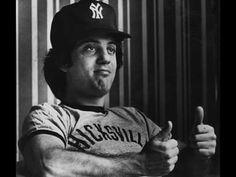 a man in a baseball uniform giving the thumbs up sign with his right hand while sitting at a table