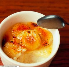 a bowl filled with bananas and ice cream on top of a wooden table next to a spoon