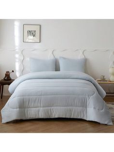 a white bed with blue comforter and pillows on top of it in a room