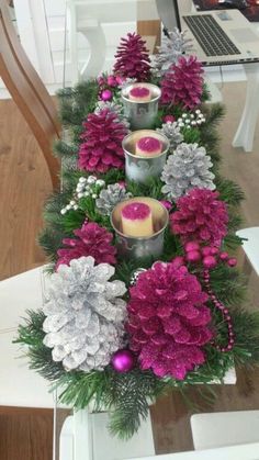 some candles are sitting on a table with pink flowers and pineconis in the center