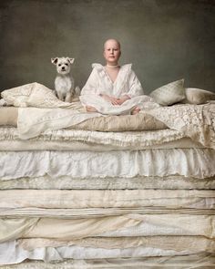 a woman sitting on top of a bed next to a small white dog in front of her