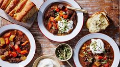 three bowls of stew with bread and sour cream on the side, along with other dishes