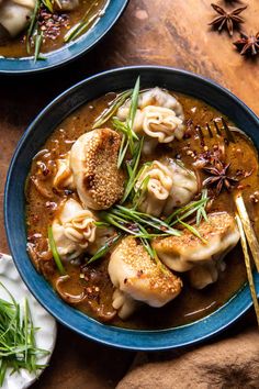 two blue bowls filled with dumplings and sauce on top of a wooden table next to an orange napkin