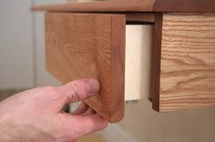 a hand is holding the door handle on a wooden cabinet with a drawer in it