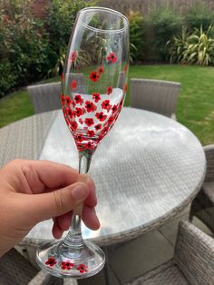 a hand holding a wine glass with red and white flowers painted on the outside rim