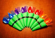 colorful plastic forks and spoons are arranged in a row on top of a wooden table