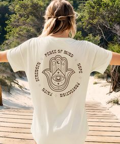 a woman standing on a wooden walkway with her arms spread out to the side wearing a white tee shirt that says peace of mind