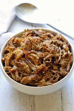 crockpot carnitas in a white bowl with spoons on the side