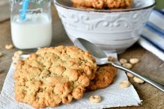 two cookies on a napkin next to a bowl of peanuts and a glass of milk