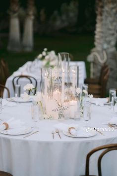 the table is set with white flowers and candles in glass vases, plates and napkins