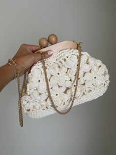 a woman's hand holding a white crocheted purse with two wooden beads