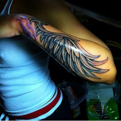 a woman's arm with an angel wing tattoo on the upper half of her arm