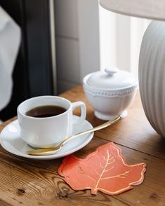 a cup of coffee sits on a table next to a plate with a leaf shaped coaster