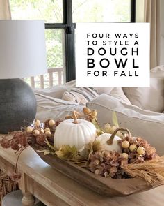 a wooden tray filled with white pumpkins on top of a table next to a lamp