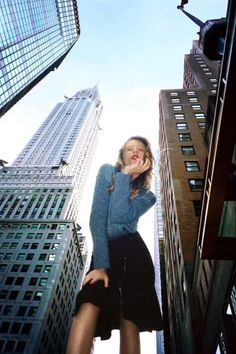 a woman standing in the middle of tall buildings with her hands on her hips and looking up at the sky