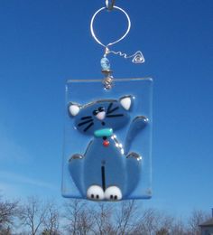 a glass ornament with a cat on it hanging from a chain in front of a blue sky