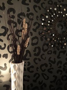 a white vase filled with dry grass next to a leopard print wallpapered wall