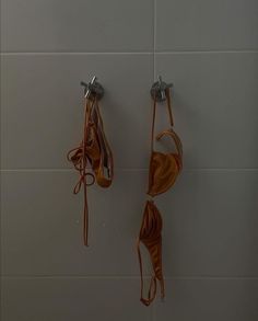 two brown bras hanging from hooks on a white tiled wall