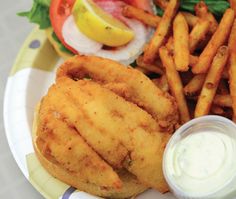 fish and fries on a plate with ketchup, tomatoes, lettuce and lemon wedges