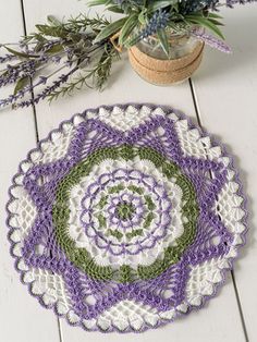 a crocheted doily with purple and green flowers in the center on a white wooden surface