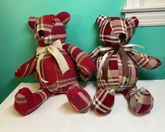 two red teddy bears sitting next to each other on a white counter in front of a green wall