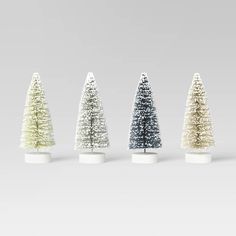 four small christmas trees are lined up in different colors and sizes, with white bases