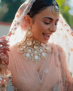 a woman in a bridal gown smiles and holds her veil up to her head