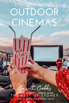 a person holding up a red and white popcorn bucket with the words sydney summer outdoor cinemas on it