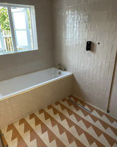 an empty bathroom with a bathtub and tiled floor in front of a window on the wall