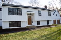 a white two story house with black shutters and wood doors on the front door