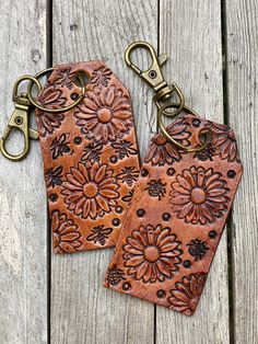 two brown leather tags with flowers on them sitting on a wooden table next to each other