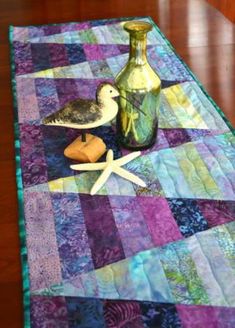 a quilted table runner with seagulls and starfish on it, along with two vases