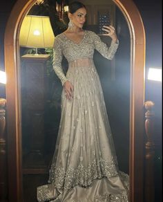 a woman taking a selfie in front of a mirror wearing a silver gown and matching earrings