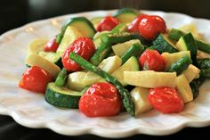 a white plate topped with cucumbers, tomatoes and green beans on top of a table