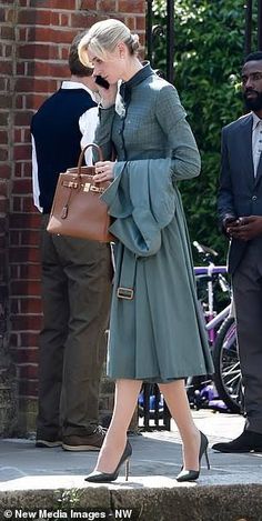 a woman in a dress and heels is walking down the street with her handbag