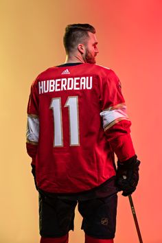 a hockey player in red jersey holding a stick and looking off to the side with his hand on his hip