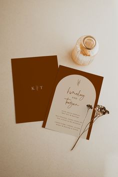 the wedding stationery is laid out next to a vase with dried flowers on it