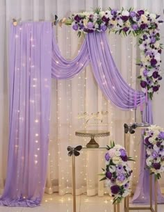 a purple and white wedding arch decorated with flowers, ribbons and lights in the background