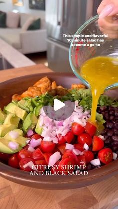 a person pouring dressing into a bowl filled with vegetables and other ingredients to make an avocado salad