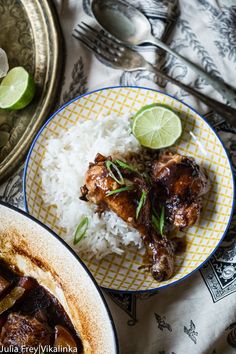 two plates filled with rice, meat and limes next to silverware on a table