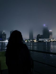 a woman is looking out over the water at night with city lights in the background