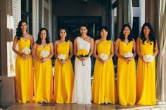 a group of women standing next to each other wearing yellow dresses and holding bouquets