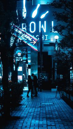 two people are walking down the sidewalk in front of a building with neon lights on it