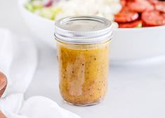 a glass jar filled with mustard sitting on top of a table next to a salad