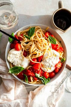 a white bowl filled with pasta, tomatoes and mozzarella on top of a table