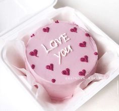 a pink cake in a white box with the words love you written on it and hearts